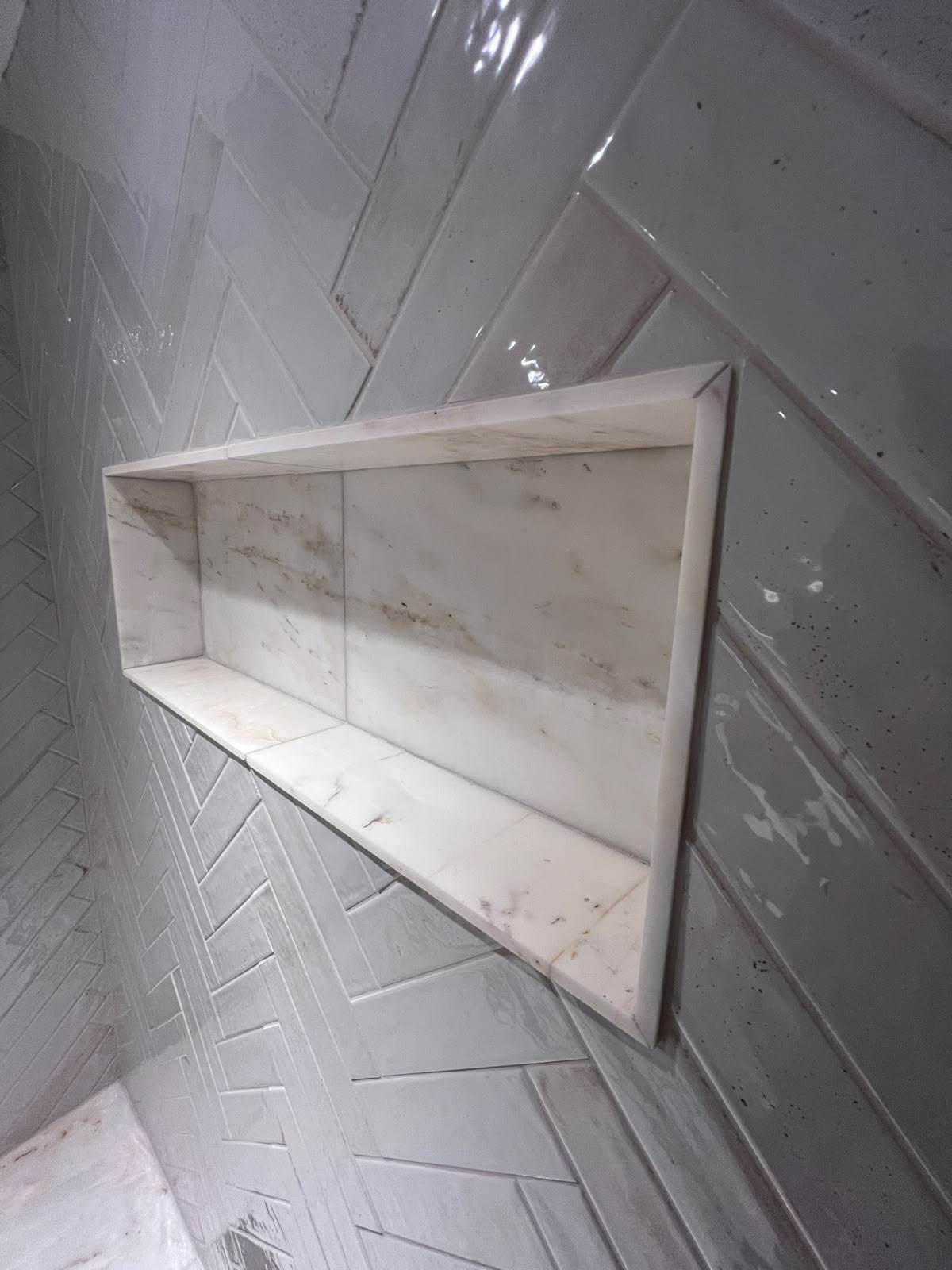 Herringbone tiling with mitred marble niche in a Kent bathroom