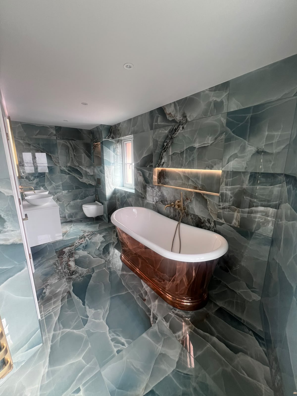 Natural stone tiling in a Kent bathroom with blue onyx-effect walls and floor