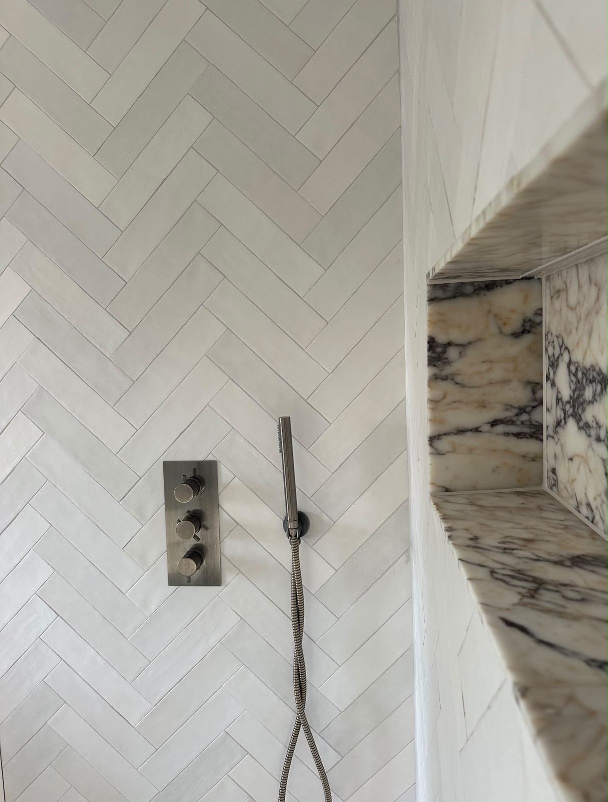 White herringbone tiled shower wall with mitred marble niche in Kent